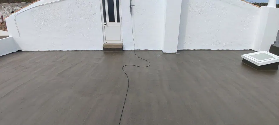 Uma fotografia que mostra um terraço impermeabilizado com a vista para uma porta e um cabo elétrico que se estende pelo chão. Esta imagem ajuda a dar uma ideia do contexto de um terraço habitável, e a forma como a impermeabilização se integra com outras estruturas.