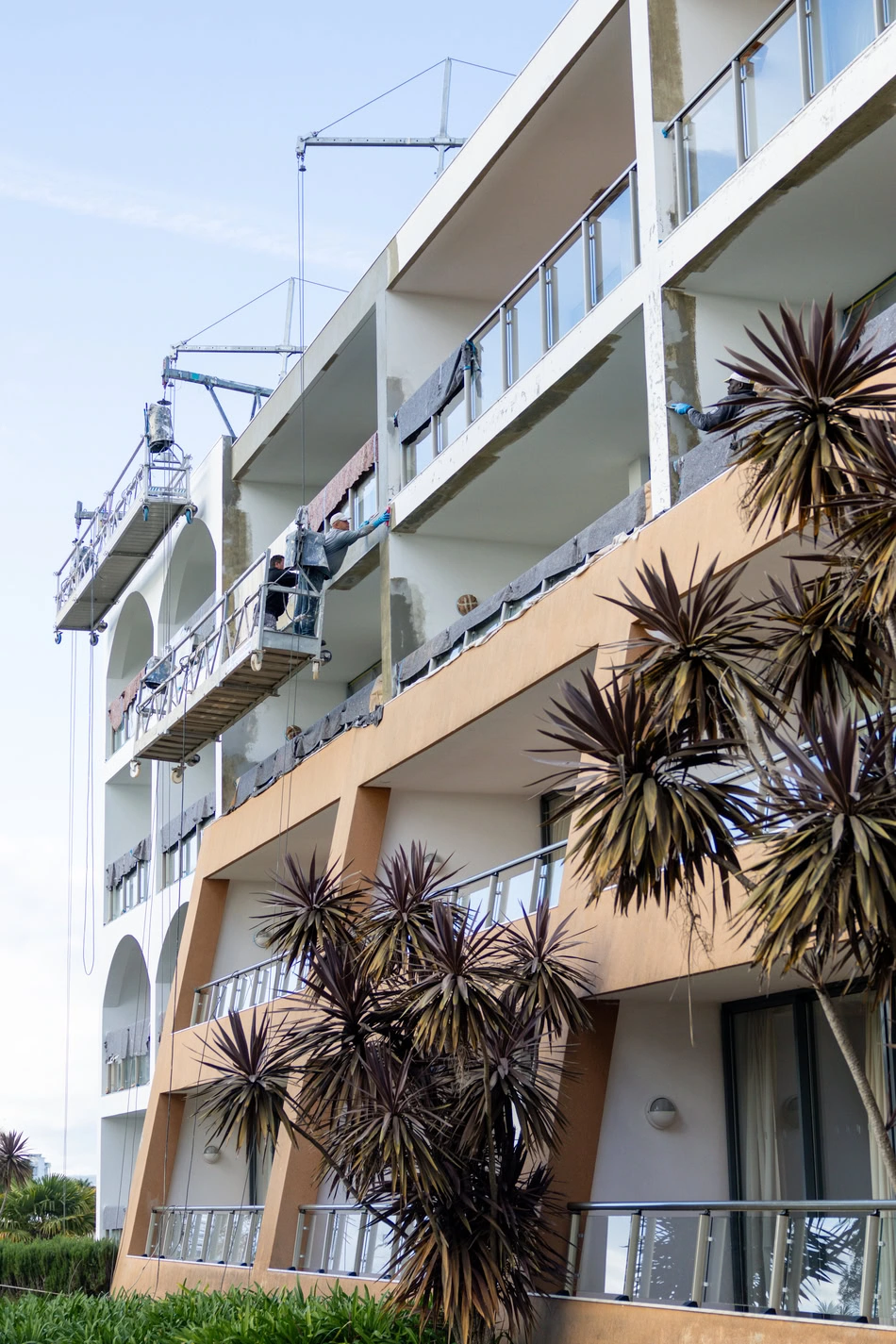 Reabilitação de fachada de hotel com andaime suspenso e trabalhador a efetuar obras. Construção civil e restauro de edifícios.