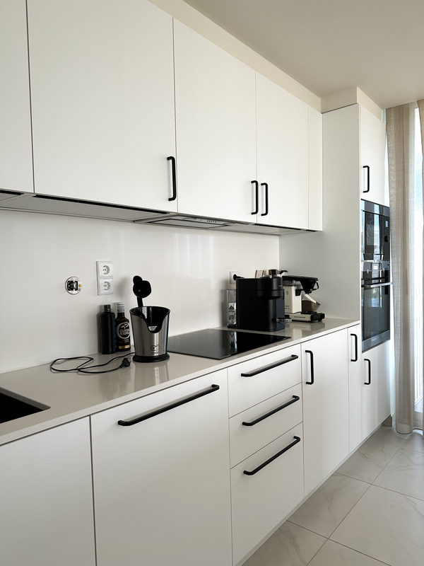 Cozinha moderna com armários em branco mate e puxadores pretos. Design de bancada minimalista e eletrodomésticos embutidos.