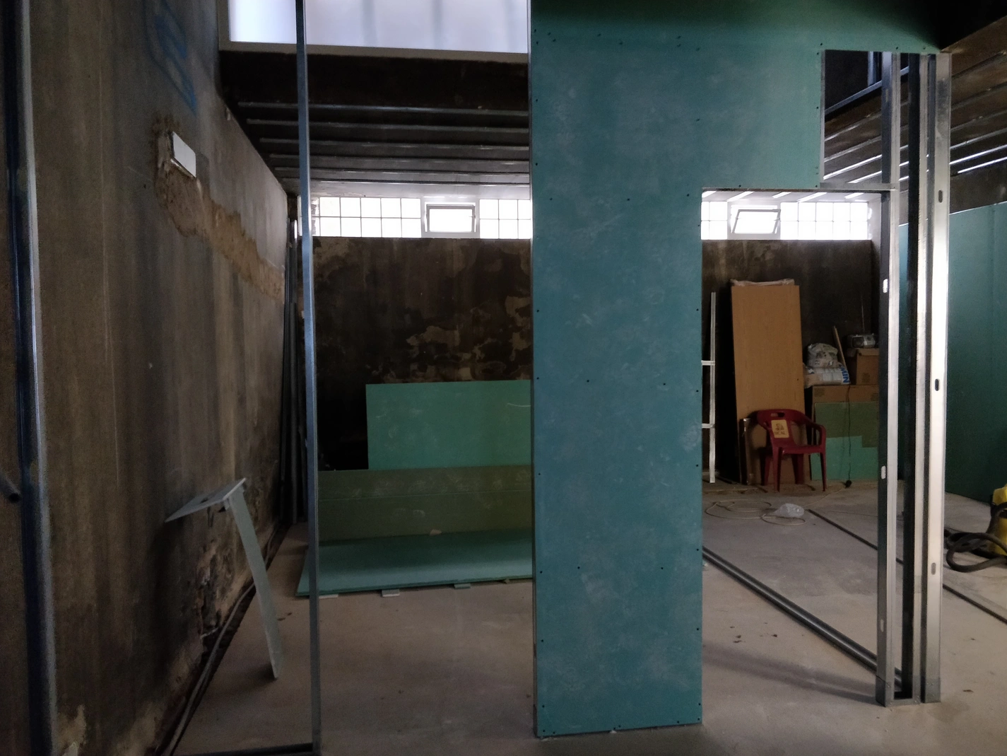 Obra de remodelação interior: parede em pladur hidrófugo (verde/azul) a criar divisória e porta. Estrutura metálica para drywall, teto falso em construção.