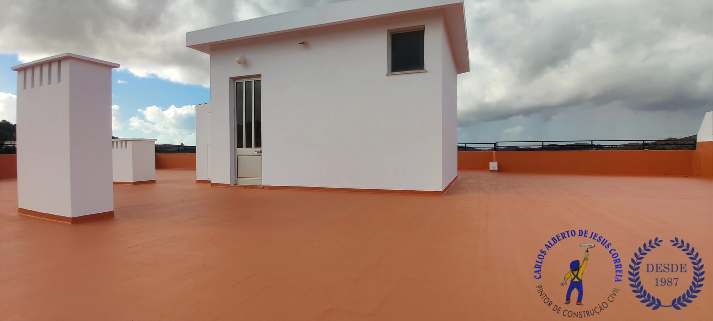 Terraço impermeabilizado em Silves, Algarve. Superfície plana e ampla de cobertura pintada em cor terracota/laranja, com revestimento impermeabilizante. No centro, uma estrutura branca retangular (acesso ou casa das máquinas) com uma porta envidraçada e uma pequena janela
